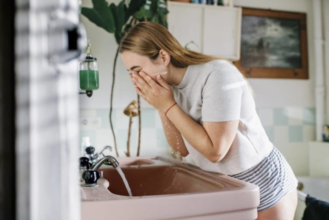 Woman in bathroom washing face comment bien se nettoyer le visage